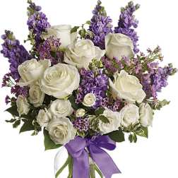 White roses and purple flowers in a glass vase with a purple ribbon