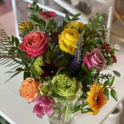 Mixed bouquet of colorful roses, gerbera daisies, and other blooms in a glass vase