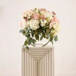 Blush and white floral arrangement on a pedestal with trailing greenery