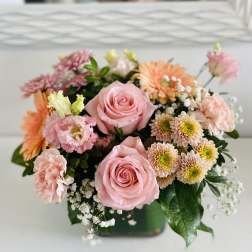 Pink roses and mixed pastel flowers arranged in a low square vase