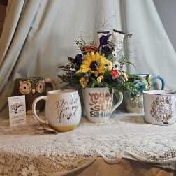 Flower arrangement in a mug surrounded by decorative quote mugs