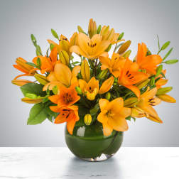 Orange lilies arranged in a round green glass vase