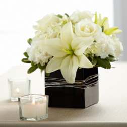 Low white lily and rose arrangement in a black square vase with votive candles