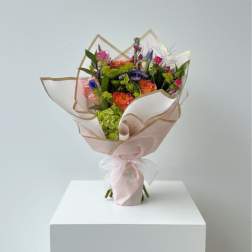 Bouquet of orange, pink, and purple flowers wrapped in pale pink paper