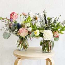 Two mixed flower arrangements in clear glass vases on a stool