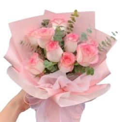 Handheld bouquet of pink roses wrapped in pale pink paper