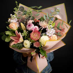 Mixed bouquet of pink, peach, and white flowers wrapped in pink paper