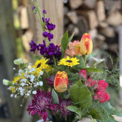 Mixed bouquet with purple, yellow, and pink flowers in a white pitcher vase