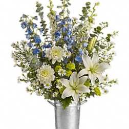 White lilies and blue flowers arranged in a silver bucket vase