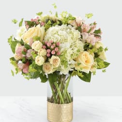 Bouquet of cream and pink flowers in a clear vase with a gold wrap
