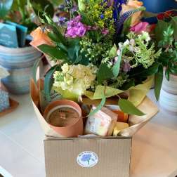 Mixed bouquet with peach roses, purple flowers, and a candle gift box in a cardboard box