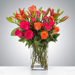 Bouquet of pink and orange roses, lilies, and carnations in a clear glass vase