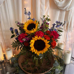 Sunflowers, red roses, and purple flowers in a glass vase