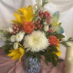 Mixed bouquet with yellow lilies, orange roses, and white chrysanthemums in a patterned vase