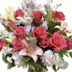Pink roses and lilies arranged in a glass vase with lavender flowers