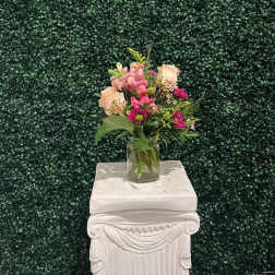 Small mixed flower arrangement in a clear glass vase on a white pedestal