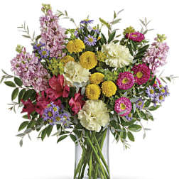Mixed bouquet of pink, yellow, white, and purple flowers in a glass vase
