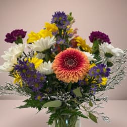 Mixed bouquet in a glass vase with purple, yellow, white, and peach flowers.