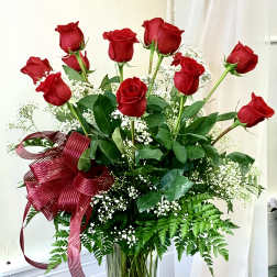 Red roses in a clear glass vase with white baby's breath and a burgundy ribbon