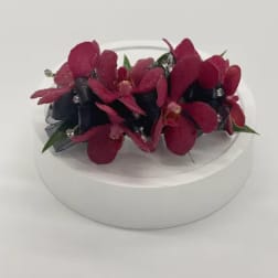 Red orchid wrist corsage with black ribbon and rhinestone accents on a white stand