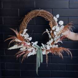 Asymmetrical dried floral wreath with white accents and sage ribbon on a grapevine base.