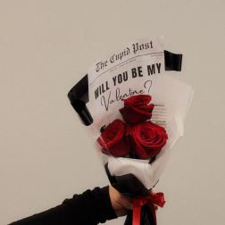 Handheld bouquet of red roses wrapped in black and white paper