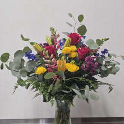 Mixed bouquet of roses, lilies, and purple flowers in a clear glass vase