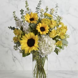 Yellow sunflowers and white flowers arranged in a clear glass vase