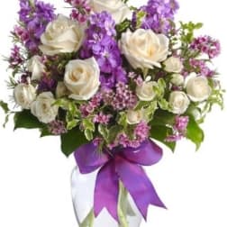 White roses and purple flowers arranged in a clear glass vase with a purple ribbon