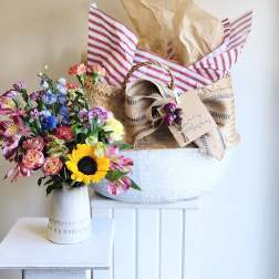 Mixed bouquet in a white vase beside a wrapped gift basket