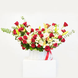 Red roses and white orchids in a white basket with a red ribbon