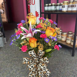 Mixed bouquet with roses, lilies, and a leopard-print bow in a glass vase