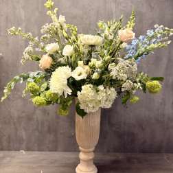 Tall floral arrangement in a pedestal vase with white, peach, and blue blooms