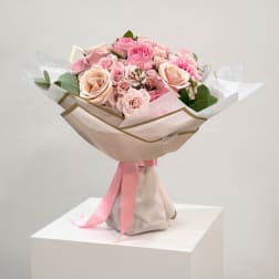 Pink and blush rose bouquet wrapped in pale paper with a pink ribbon