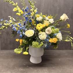 Blue and yellow mixed flower arrangement in a white vase
