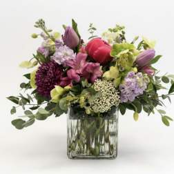 Mixed bouquet of pink, purple, and green flowers in a square glass vase