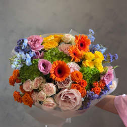 Mixed bouquet of orange, pink, yellow, and blue flowers wrapped in pale paper