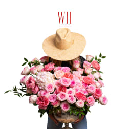 Large bouquet of pink roses in a glass vase held by a person wearing a straw hat.