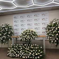 Large white rose funeral sprays and a floor arrangement displayed indoors