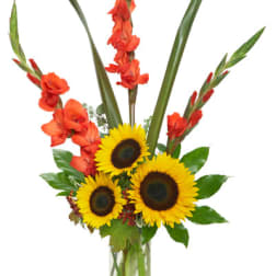 Tall arrangement of yellow sunflowers and orange gladiolus in a clear glass vase