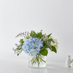 Blue hydrangea bouquet in a clear glass vase with white blooms