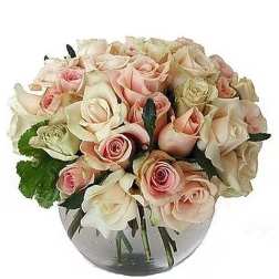 Low round arrangement of blush and cream roses in a clear glass bowl vase