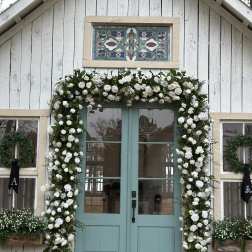 White rose garland framing a teal double door on a white cottage
