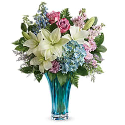 Bouquet of lilies, roses, and hydrangeas in a blue glass vase