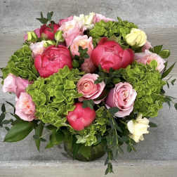 Round arrangement of pink roses, coral peonies, and green hydrangeas in a glass vase