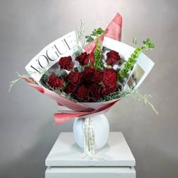 Bouquet of deep red roses wrapped in pink paper and magazine pages in a white vase