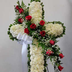 White floral cross with red roses and a white ribbon on a stand