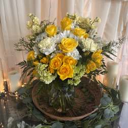 Yellow roses and white flowers in a glass vase with candles