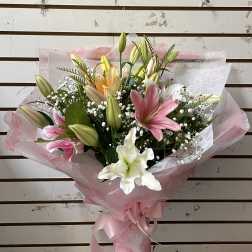 Bouquet of pink, white, and yellow lilies wrapped in pink paper
