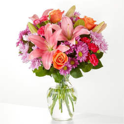 Pink lilies, orange roses, and purple daisies in a glass vase